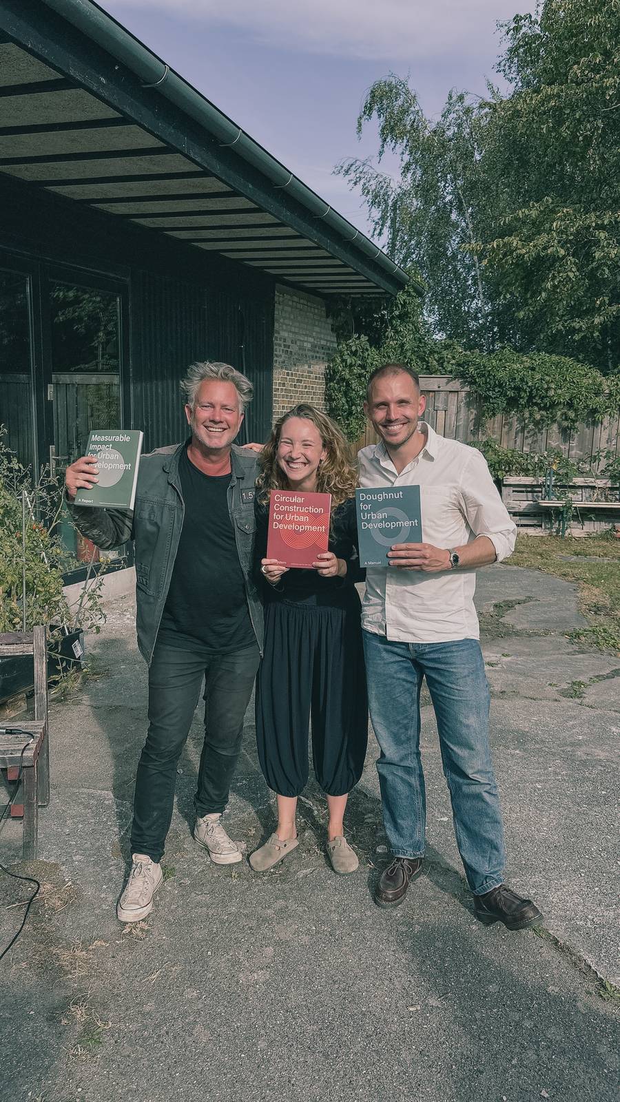 Tre kolleger holder hver sin af vores tre udgivelser op foran kontoret.